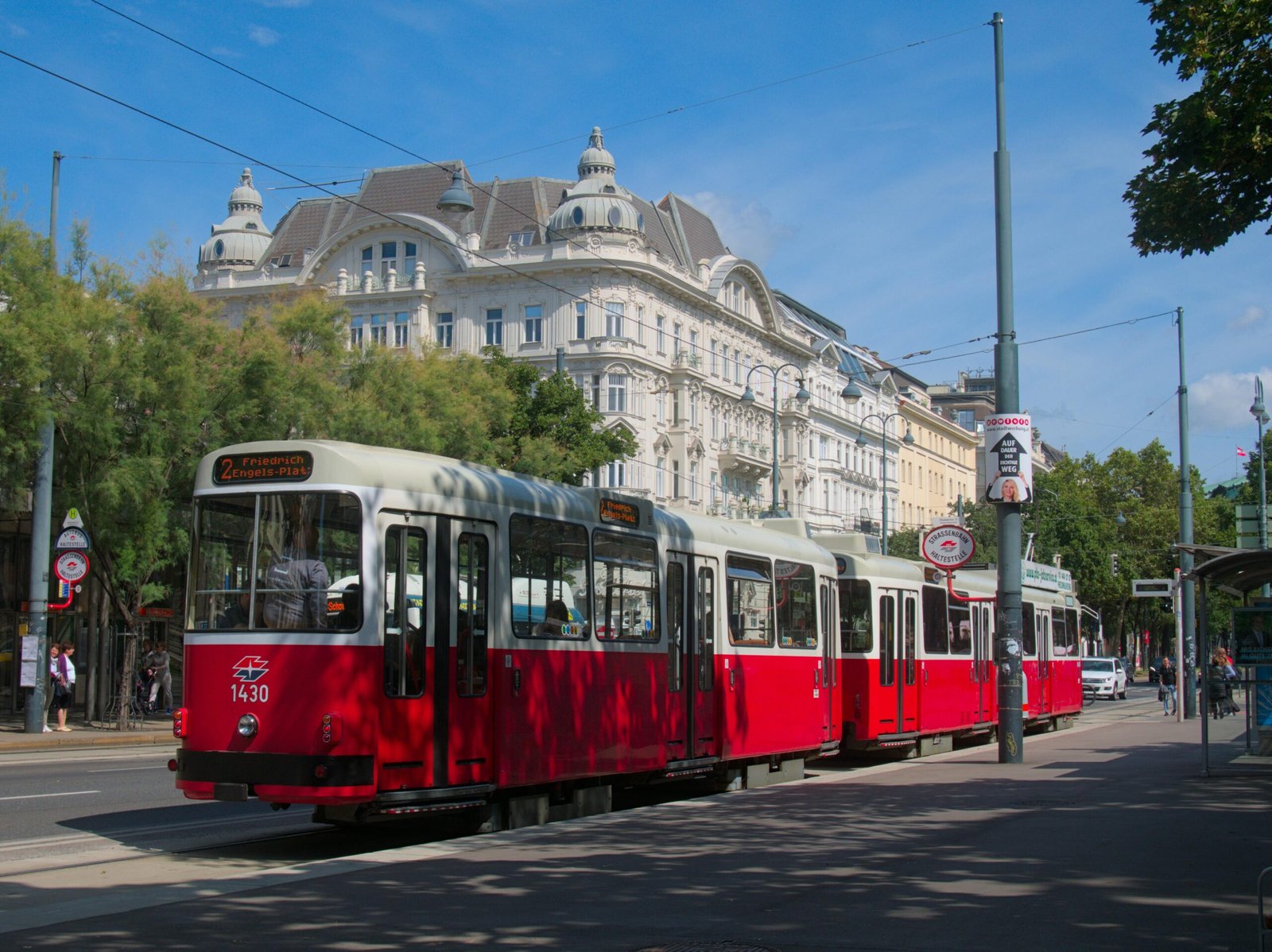 Iconic red tram traverses scenic city streets of Vienna, Austria against a bright blue sky.